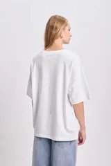 Remera blanca de corte amplio con estampado abstracto de flores en tonos rosa, rojo y verde.