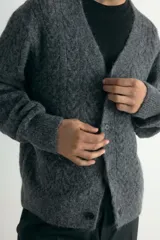 Saco gris de punto trenzado con escote en V pronunciado y botones frontales. Presenta remate acanalado en cuello, tapeta, puños y bajo. Corte holgado.