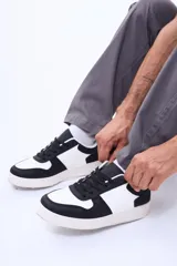 Championes urbanos de diseño bicolor en blanco y negro, con cordones negros y suela de goma en tono crema. Presentan una estructura robusta con refuerzos en puntera, talón y laterales.