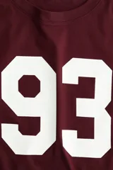 Remera de manga corta color bordó, con cuello redondo y corte holgado. Estampado grande con el número "93" en color blanco en el frente.