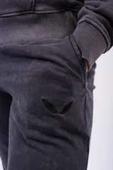 Pantalón de jogging color gris oscuro con efecto lavado, confeccionado en frizza de algodón. Presenta un diseño relajado con bolsillos laterales y un detalle bordado de alas en la parte frontal.