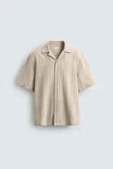 Camisa de manga corta y corte relajado, confeccionada en tejido de algodón con estructura de rayas verticales. Presenta cuello bowling, cierre frontal con botones y aberturas laterales en el bajo.