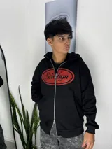 Campera negra con capucha y cierre frontal completo. Presenta un estampado ovalado en color rojo en el pecho con la inscripción Scrdsgn.