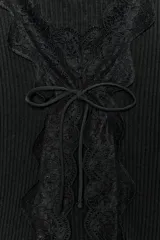 Top de punto rib negro con escote en pico, manga larga y cierre frontal con lazadas. Presenta detalles de encaje a tono en los bordes del escote y la abertura frontal.