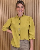 Camisa mostaza de algodón, con cuello alto con volados, botonadura frontal y mangas tres cuartos con puños también con volados.