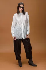 Camisa blanca de corte holgado, con cuello clásico y cierre frontal de botones. Presenta un delicado bordado de mariposas en toda la prenda y mangas largas con puños abotonados.