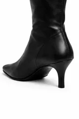 Botas altas de caña media en eco cuero negro, con taco fino de 4 cm y punta fina. Presentan un diseño distintivo en la parte posterior con una hilera de ganchos metálicos tipo imperdibles plateados.