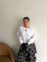 Remera de manga larga color marrón, con cuello redondo y detalle de parche cuadrado con logo bordado en el centro del pecho. Presenta un corte holgado y diseño minimalista.