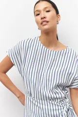 Vestido corto a rayas verticales azules y blancas, de corte suelto y manga corta. Presenta un lazo en uno de sus laterales.