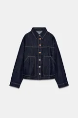 Cazadora de denim en color azul oscuro con costuras en contraste, cuello solapa, manga larga y cierre frontal con botones metálicos. Presenta dos bolsillos de plastrón en el delantero.