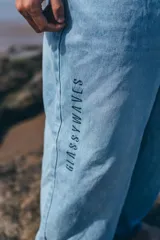 Pantalón de jean corte loose fit color celeste claro, con diseño de cinco bolsillos y estampa vertical con la frase 'GLASSYWAVES' en la pierna derecha.