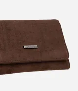 Billetera femenina de tamaño mediano con formato sobre y estructura firme. Presenta un acabado texturizado en color marrón y cuenta con una placa metálica decorativa con el logo de la marca en la parte frontal.