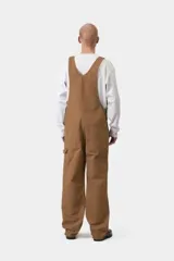 Mameluco Carhartt WIP modelo Bib Overall, de color negro, con múltiples bolsillos frontales, tirantes ajustables con hebillas metálicas y el parche con el logotipo de la marca en el bolsillo del peto.