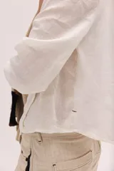 Blusa blanca de lino con escote en V y mangas largas con puños elásticos, combinando delantera estructurada de lino y espalda de algodón con spandex.