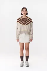 Buzo de tejido de punto en color azul marino, con cuello alto y cierre frontal parcial. Presenta un diseño con franjas en color marrón y detalles de líneas en rojo en el pecho, hombros y ruedo. Tiene corte holgado y mangas largas con puños acanalados.