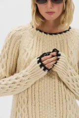 Sweater de punto de mohair color beige, con cuello redondo, mangas largas y detalles de terminación en color negro en el cuello, puños y ruedo.