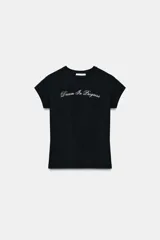 Camiseta negra de manga corta y cuello redondo, con texto bordado en blanco en el pecho que dice "Dream In Progress" en tipografía cursiva.