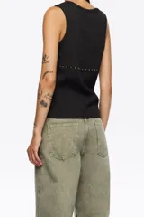 Camiseta sin mangas negra, de tejido acanalado, con escote redondo y una hilera de remaches metálicos plateados a la altura de la cintura.