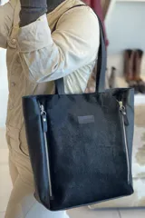 Bolso tipo tote de cuero negro con textura de pelo en el frente y cierres laterales.