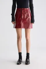 Minifalda evasé de tiro alto, confeccionada en material sintético de acabado brillante, estilo charol, con diseño de cinco bolsillos y cierre frontal con botón y cremallera.