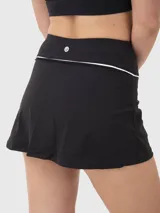 Conjunto deportivo compuesto por un top corto con cuello polo y una pollera short (skort) con detalle de línea blanca en la cintura. Ambas piezas son de color negro y diseño minimalista.