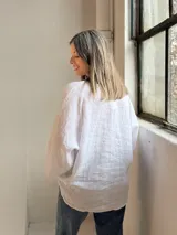 Camisa blanca de lino, con cuello en V, cierre frontal de botones y mangas amplias de corte holgado.