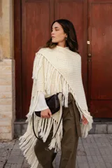 Poncho triangular de lana en color crudo, con diseño de tejido texturizado y terminaciones de flecos largos en todo el borde.