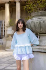 Blusa celeste de tela liviana con escote cuadrado, mangas tres cuartos amplias y detalle de volado horizontal en la parte frontal.