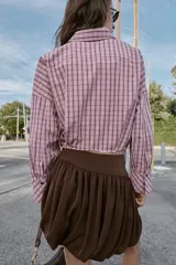 Camisa de manga larga con estampado de cuadros en tonos rosados y negros. Presenta cuello solapa, bolsillo delantero de plastrón, cierre frontal con botones y detalle de laterales ajustables con lazos.