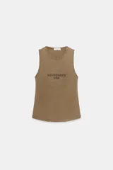 Musculosa de algodón con cuello redondo y manga sisa. Presenta un diseño frontal con forma de estrella delineada por tachas metálicas y texto estampado en el centro.