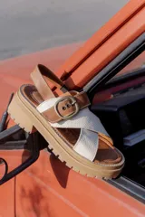 Sandalias de plataforma con suela track, combinando cuero liso color tostado y cuero texturizado color crema. Presentan tiras cruzadas en el empeine, una tira trasera ajustable con hebilla metálica envejecida y costuras a la vista.