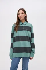 Remera tipo polo de manga larga con diseño de rayas horizontales anchas en bloques de color crema y beige. Presenta cuello camisero con cierre de botones y un pequeño bordado en el pecho.