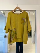 Blusa color mostaza de corte holgado y manga corta, con detalles de apliques estampados con motivos botánicos en el bolsillo pectoral y en el lateral inferior.