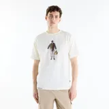 Remera de manga corta New Balance Varsity para hombre, de color blanco marfil con calce relajado y cuello redondo. Presenta un estampado gráfico central con diseño ilustrado y texto bordado en el borde inferior.