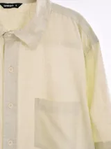 Camisa de manga corta color blanco roto con textura de tejido de lino o similar, corte holgado y cuello camisero.