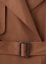 Chaqueta larga tipo trench color marrón, con diseño recto, solapas anchas, doble botonadura, bolsillos laterales y cinturón desmontable de la misma tela.