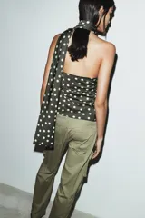Top de tejido satinado con estampado de lunares, diseño de cuello halter tipo foulard y detalle de frunces laterales. Cuenta con cierre lateral mediante cremallera oculta.