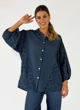 Camisa azul marino de algodón, con diseño oversize, cuello camisero, cierre frontal con botones blancos y mangas abullonadas con detalles de bordado inglés y perforaciones.