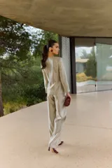 Blazer corto de satén color beige dorado, con escote en V profundo, hombreras y un lazo grande integrado en la cintura para anudar al frente. Presenta mangas largas de corte recto.