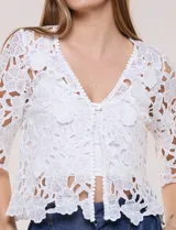 Bolero corto de encaje blanco con motivo floral y transparencias, escote en V pronunciado y mangas tres cuartos.