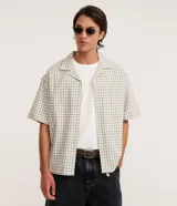 Camisa de manga corta para hombre con diseño boxy, confeccionada en tricolina de algodón con estampado de cuadros y textura sutil. Presenta cuello camisero, cierre frontal con botones y un bolsillo aplicado en el pecho.
