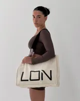 Bolso tipo tote bag de algodón color crudo, con asas negras y estampado frontal con la palabra "LON" en letras negras grandes.