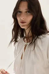 Blusa de algodón de corte holgado, con cuello redondo fruncido y cierre de lazo frontal. Presenta mangas largas con puños elásticos.