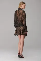 Camisa negra de encaje semitransparente con diseño floral, cuello camisero y mangas largas.