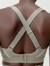 Top deportivo color beige con tirantes regulables cruzados en la espalda y cierre ajustable. Presenta una banda reflectante en el frente y copas extraíbles.