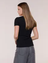 Remera básica de modal elastizado color blanco, con textura acanalada fina, escote redondo y mangas cortas. Presenta un pequeño logo metálico aplicado cerca del ruedo frontal.