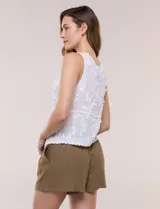 Blusa sin mangas blanca de puro algodón liviano, con escote en V, bordados florales en relieve, cartera frontal abotonada y terminaciones con festón calado.