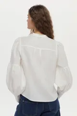 Camisa de lino color beige, con escote en V, cuello mao y mangas abullonadas tres cuartos. Cuenta con cierre frontal de botones y tiras ajustables para atar en la cintura.