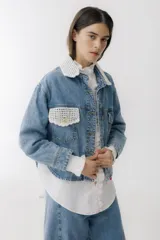 Campera de jean azul con detalles de tejido crochet en color blanco en el cuello y en uno de los bolsillos frontales. Posee cierre frontal con botones metálicos y un corte clásico.