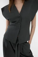 Chaleco de sastre con escote en V, cierre frontal con botones y diseño de hombros caídos. Presenta un estampado de raya diplomática sobre fondo gris oscuro.